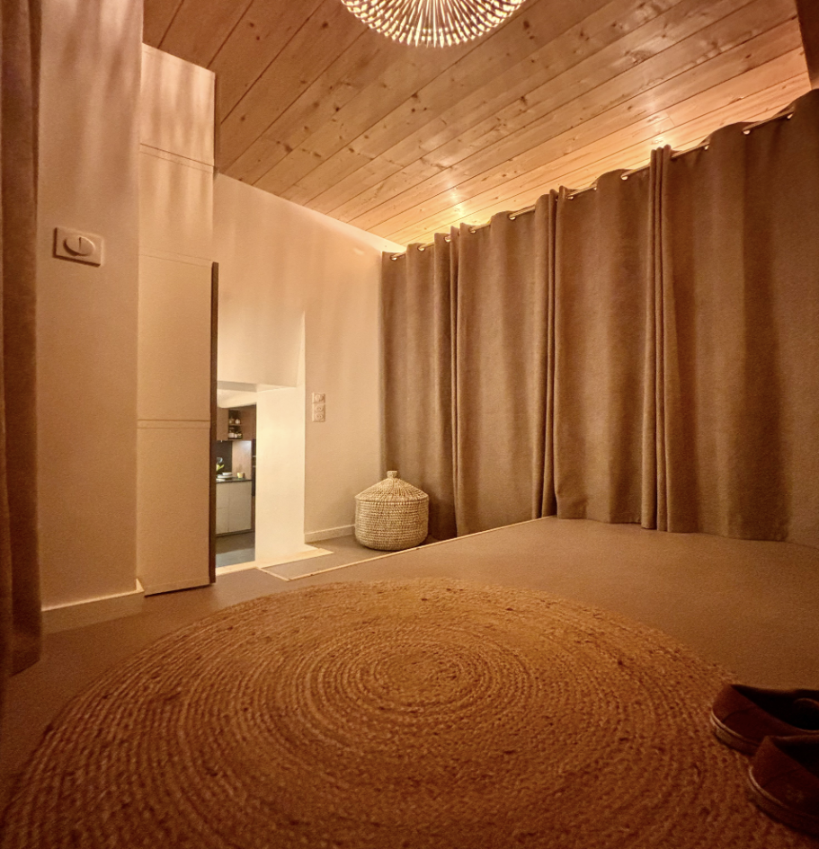 Intérieur d'une pièce avec un sol en jute, rideaux beiges et un plafond en bois.